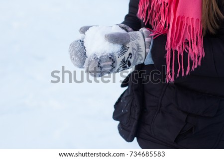 A teenage girl is holding in her hands, dressed in woolen mittens, snow in the winter.