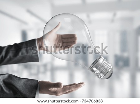 Closeup shot of business woman hands holding lightbulb with office view on background. Mixed media.