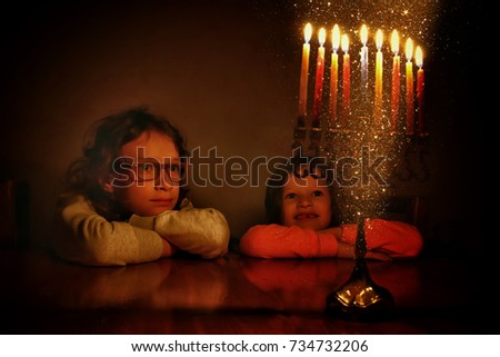 image of jewish holiday Hanukkah background with two cute kids looking at menorah (traditional candelabra) and burning candles
