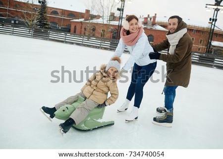 Joyful family of three having fun on skating rink on winter day