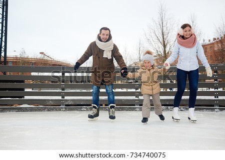 Happy couple and their daughter on skates moving down ice-rink in urban environment
