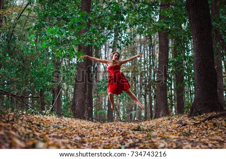 blonde walks in the woods , she is wearing a red dress . the girl is dancing