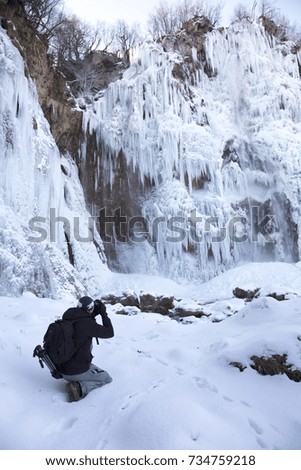 Photographer taking photo of big waterfall during winter in Plitvice lakes national park in Croatia