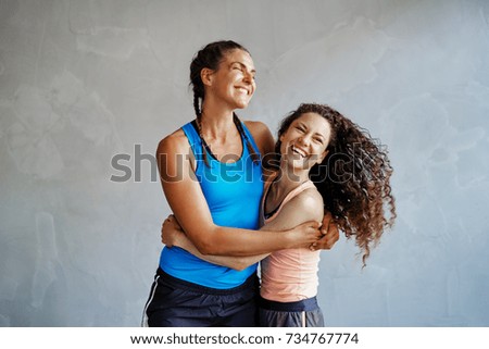 Two young women in sportswear laughing and standing arm in arm together in a gym Royalty-Free Stock Photo #734767774