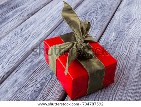 Christmas gift on wooden table. Box wrapped in red paper and tied with satin ribbon. Time to give presents.