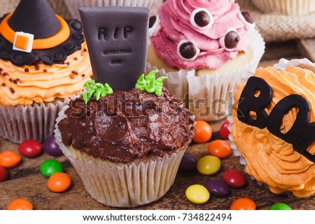 Halloween cupcakes with decorations: tombstone, eyes and pumpkin made from confectionery mastic, soft focus background