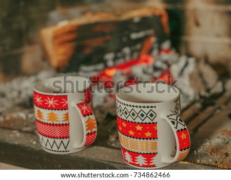Two cups stand on the fireplace opposite the fire