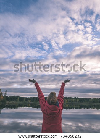 young woman in red jacket enjoying freedom in nature by the lake with cloud reflections. praise the sky. Latvia - vintage film look
