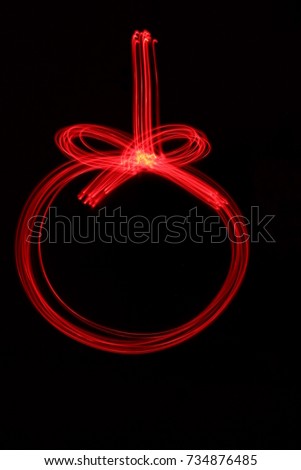 Light painting photography, red hanging bauble Christmas decoration outline, long exposure photo against a black background