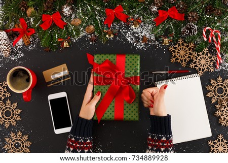 Getting online delivery of christmas gift. Woman holding holiday present, wish list, credit card and smartphone on table with xmas decoration, top view, copy space