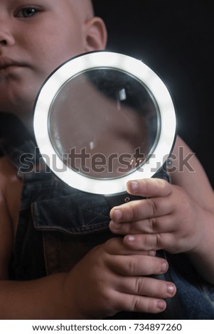 Caucasian boy playing with magnifying glass with backlight.