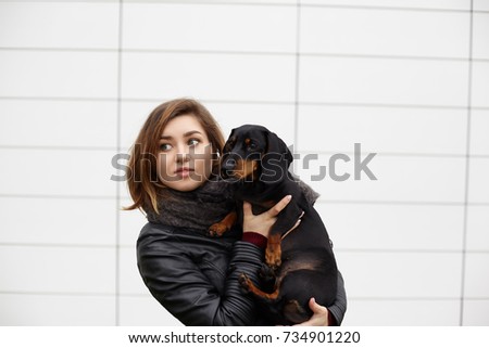 Picture of attractive young woman dog owner posing with her lovely four legged friend at blank tile wall with copy space for your text of advertising content. Blue eyed girl hugging her pet dog