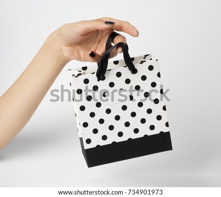 Female hand holding a white gift bag, with white polka dots on it. White background