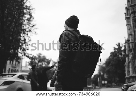 Picture of a guy standing outside on the street. We can't see his face. Young man has a big backpack so we can tell that he is a traveller. This time he is in a big city.