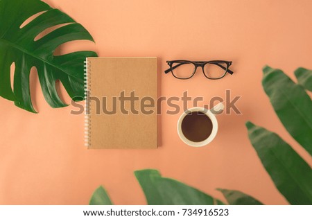 Happy break time with Notepad, Coffee cup, Tropical palm monstera leaves and Glasses on cream orange paper background. Top view with copy space. Relax with coffee concept.