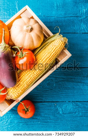Picture from above of wooden box with autumn vegetables on blue wooden table