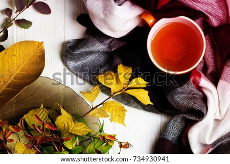 autumn picture with yellow, red and orange leaves, a cup of tea, a scarf. Cup of tea and autumn leaves on a white wooden table 