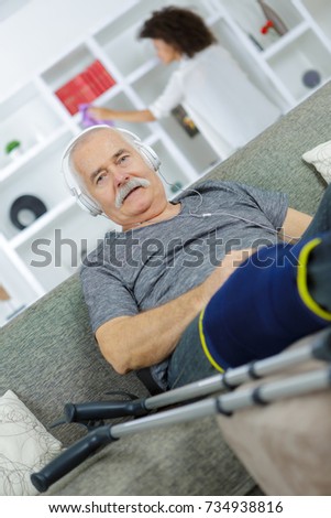 injured man listening to headphones woman doing chores in background