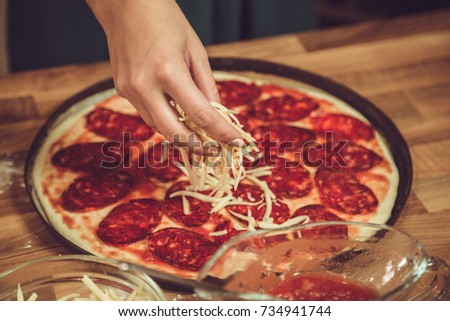 Close up of woman making pepperoni pizza and adding cheese.