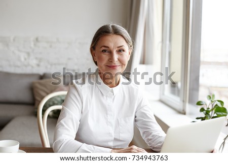 Portrait of happy skilled middle aged woman life coach, business consultant, psychologist or medical advisor smiling joyfully at camera, working on laptop, enjoying her job, helping people online