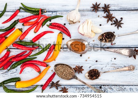Assorted set of different colors hot chili peppers, garlic, peppercorns on rustic wooden table. Mix of spices for cooking. Spicy kitchen ingredients for soups and meals.  Top view. Food background.
