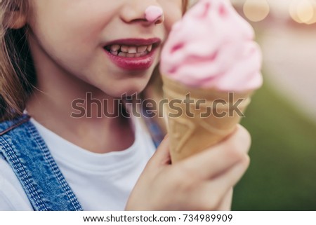 Cropped image of little pretty girl is having fun outdoor. Standing on green grass and with ice cream in hands.