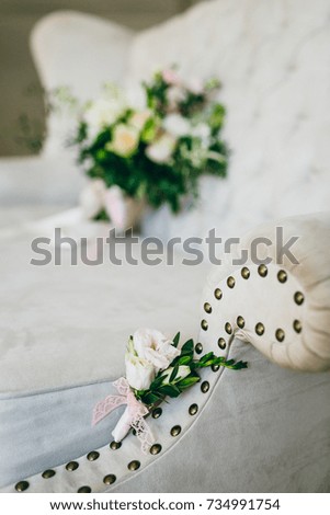 Groom's boutonniere of flowers and greens lies on the luxury sofa. Artwork