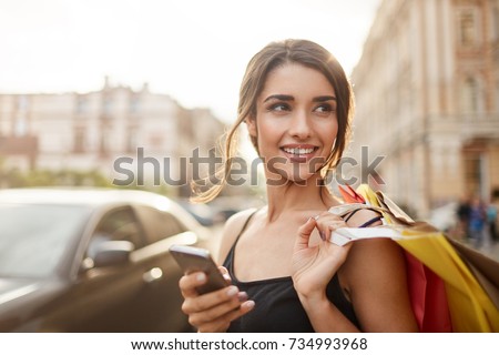 Positive emotions. Lifestyle concept. Close up of young charming dark-haired caucasian woman in black dress smiling with teeth, looking aside with relaxed expression, chatting with boyfriend on phone Royalty-Free Stock Photo #734993968