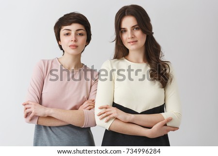 Portrait of two beautiful female university friends with dark hair, posing for graduation photo album in fashionable clothes.