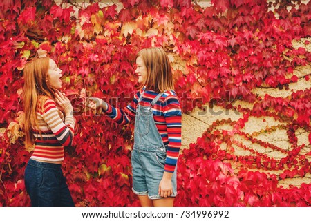 Autumn portrait of two funny girls playing together outside, posing against red ivy wall. Fall fashion for teens