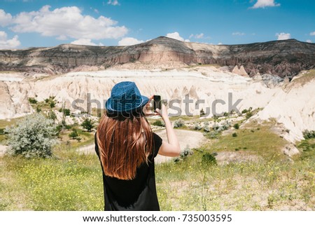A tourist girl makes a photo on the phone in memory of a beautiful view of the hills in Cappadocia in Turkey. Travel, tourism, hiking, vacation.