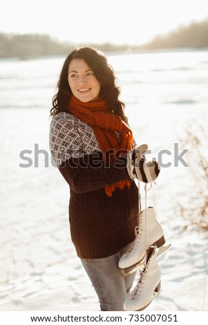 Cheerful woman carrying ice skates standing at the edge of a frozen lake