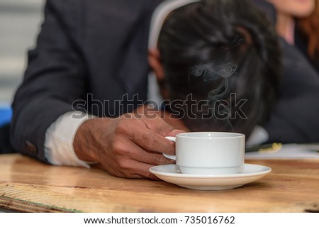 Business man feeling tired sleeping on wood table, hot coffee in white coffee cup on table.