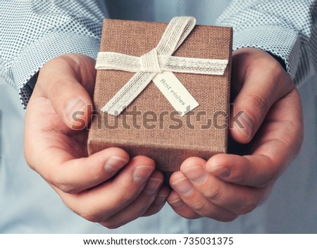 A gift in the hands of man. Close-up a brown gift box and a white ribbon with a tag. Toning and blur.