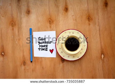A cup of coffee and give yourself more time text on a note on wooden table