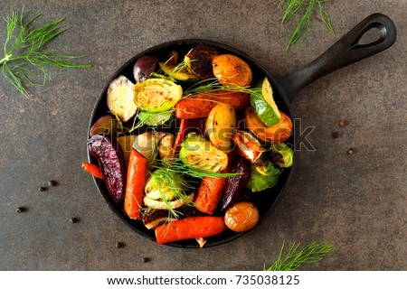 Cast iron skillet of roasted autumn vegetables, above view over a dark stone background Royalty-Free Stock Photo #735038125