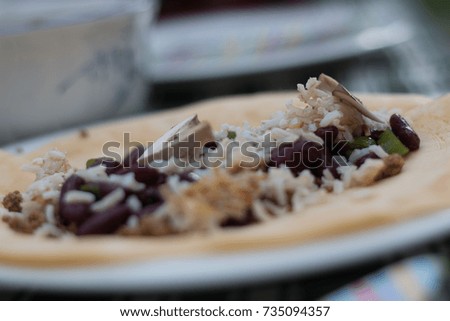 Taco or Tortilla garnish with rice, red beans, tomatoes, paprika on a wrap on plate