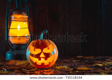 Halloween pumpkin with glowing face on a wooden background with candles.