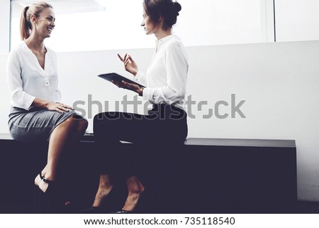 Smiling woman manager listening funny story from colleague that sitting near with portable touch pad in hand. Female entrepreneur is holding digital tablet and telling partner about successful meeting