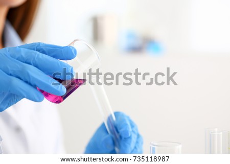 Female technician arms in protective gloves hold fluid sample bottle closeup. Medical worker in uniform use reagent tube for virus infection exam or biological toxic reaction, drug creation process