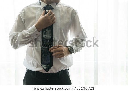 Man tying a tie in white shirt on preparation for wedding or business work