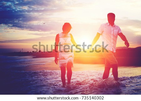 Young romantic couple walking on the beach at sunset enjoying their honeymoon vacations