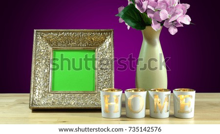 Antique photo frame with blank green screen and vase of flowers withburning home candles in elegant table interiors display
