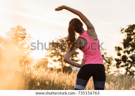 Young female workout before fitness training session at the park. Healthy young woman warming up outdoors. She is stretching her arms and looking away,hi key. Royalty-Free Stock Photo #735156763