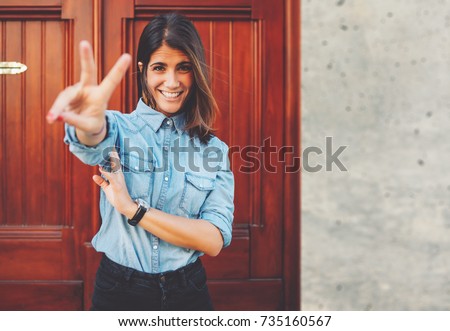 Half length portrait of the stunning young woman showing fingers peace sign with copy space area on the side of picture, attractive stylish female is having fun while posing outdoors in urban setting