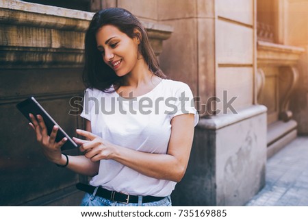 Smiling latin woman is watching photo that she just take on digital tablet camera while is walking on the street, happy female tourist is using touch pad for navigation during her summer vacation trip