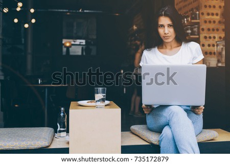 Young latin woman is sitting with open laptop in modern sidewalk coffee shop. Female freelancer is using net-book for distance work by internet connection.Student hipster girl is learning via computer