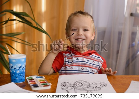 3 year old child sitting at a table and paints the coloring of the tractor with watercolors Royalty-Free Stock Photo #735179095