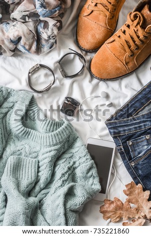 Flat lay women's clothing for autumn walks, top view. Brown suede boots, jeans, a blue pullover, scarf, bracelets, watches, headphones, perfume on a light background. Fashion concept.