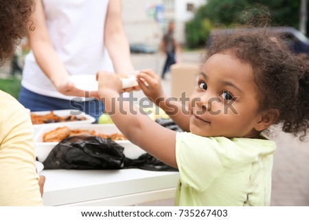 Volunteer sharing food with African child outdoors Royalty-Free Stock Photo #735267403